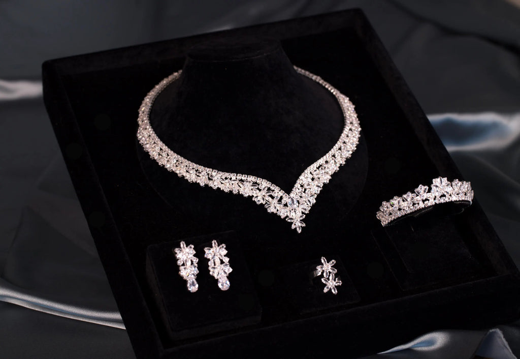Floral zircon necklace with a defined V-shaped center and coordinating earrings, bracelet and ring viewed diagonally in a black box.