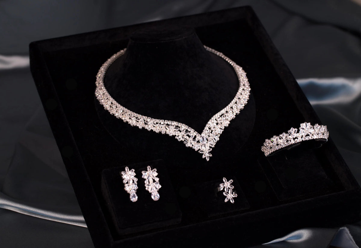 Floral zircon necklace with a defined V-shaped center and coordinating earrings, bracelet and ring viewed diagonally in a black box.