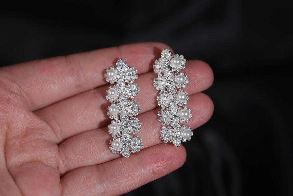 Floral faux pearl drop earrings held in a hand, showing their size and delicate silver-tone zircon details.