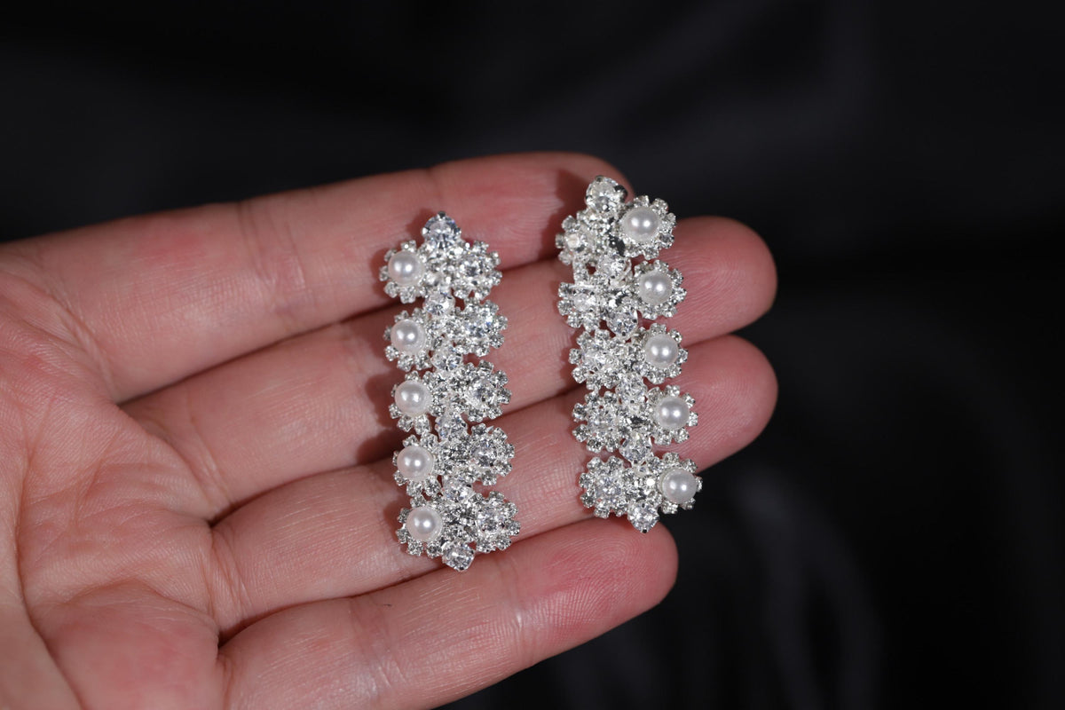 Floral faux pearl drop earrings held in a hand, showing their size and delicate silver-tone zircon details.