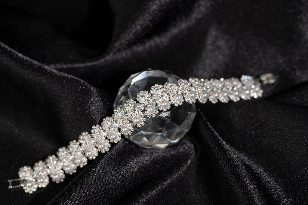 Silver-tone bridal bracelet with miniature zircon flowers and white faux pearl accents resting on black satin.