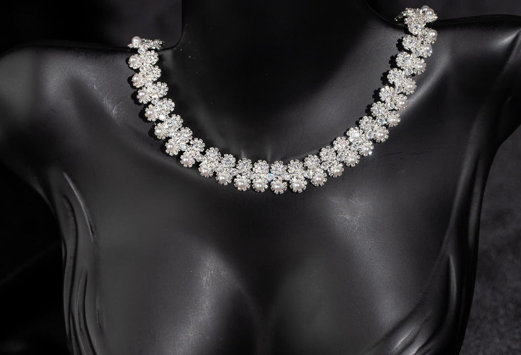 Close-up of a bridal necklace with tiny zircon flower motifs and white faux pearls following a curved neckline.
