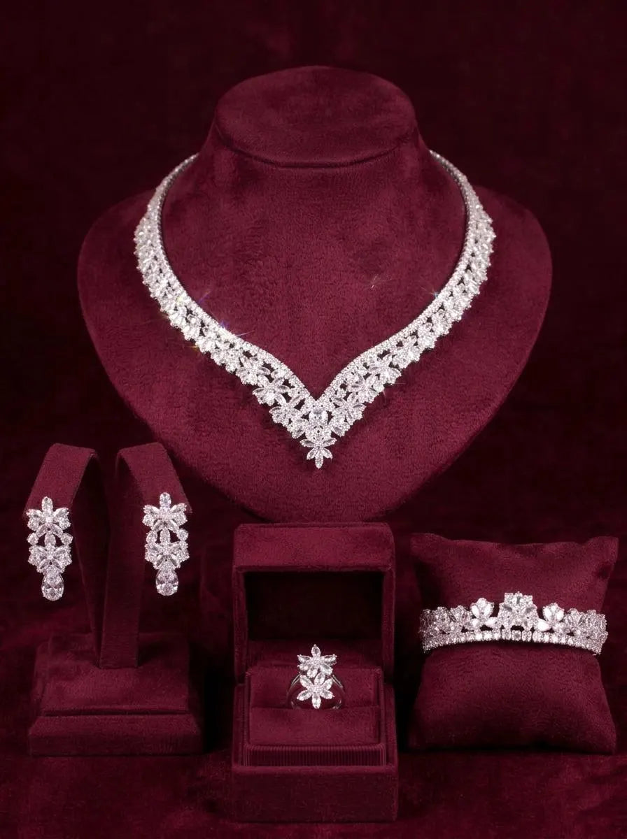 Four-piece zircon bridal jewelry set on burgundy velvet stands, featuring a V-shaped floral necklace and matching accessories.