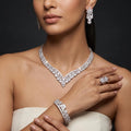 Model wearing a floral V-shaped zircon necklace with matching teardrop earrings, bracelet and flower ring in a silver-tone finish.