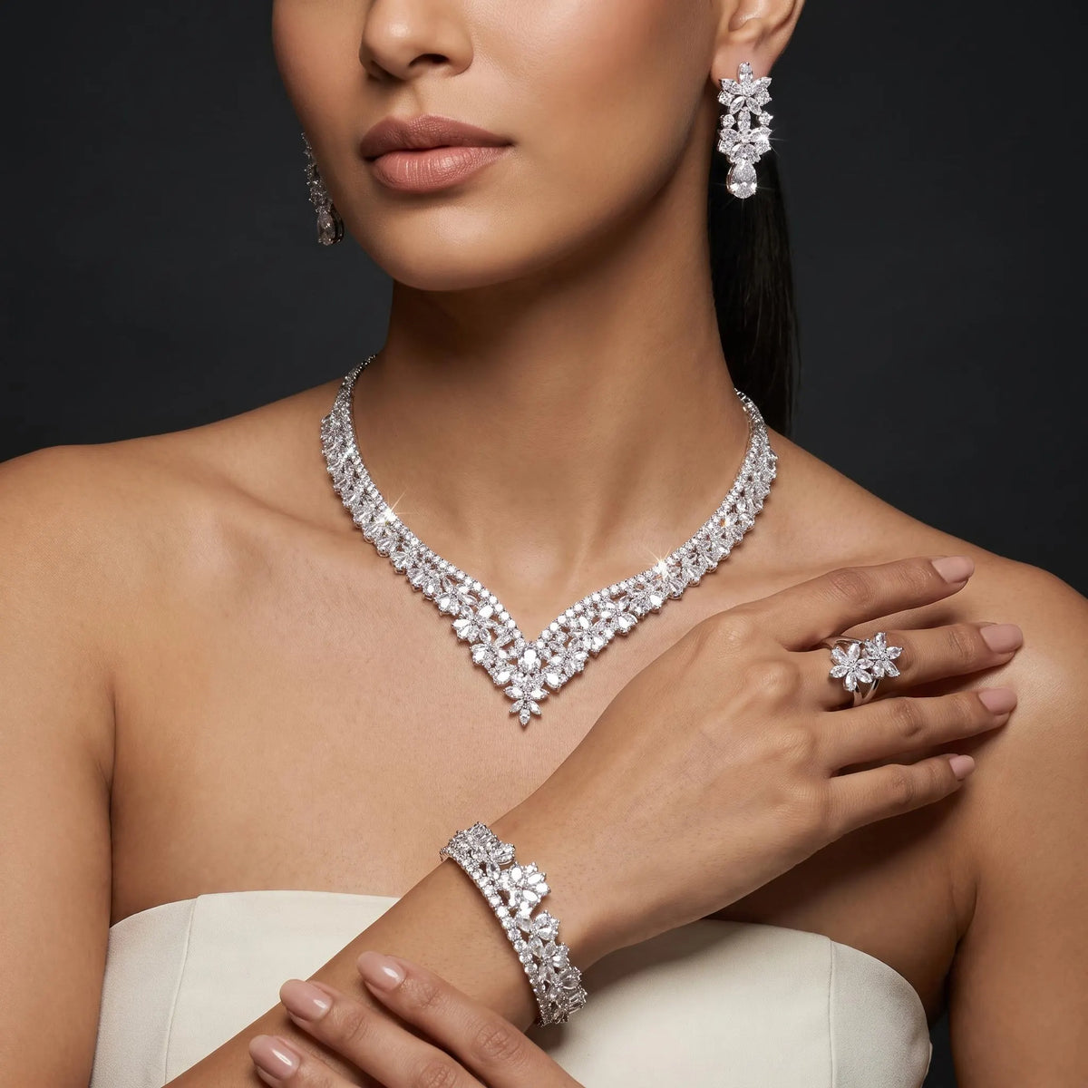 Model wearing a floral V-shaped zircon necklace with matching teardrop earrings, bracelet and flower ring in a silver-tone finish.