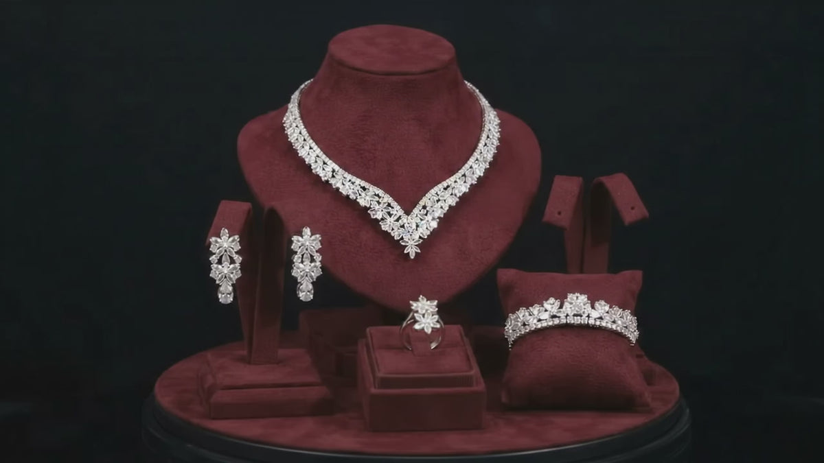 Floral V-shaped bridal necklace, teardrop earrings, bracelet and ring arranged on burgundy velvet jewelry stands.