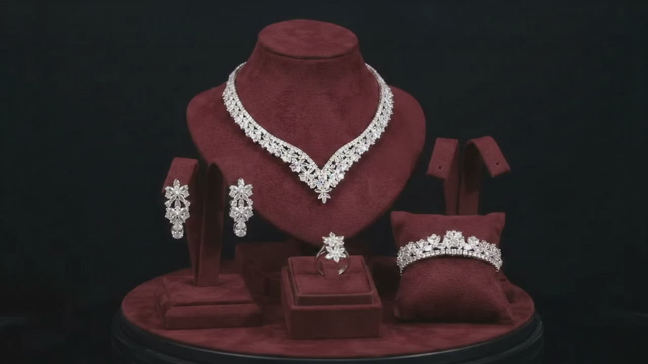 Floral V-shaped bridal necklace, teardrop earrings, bracelet and ring arranged on burgundy velvet jewelry stands.