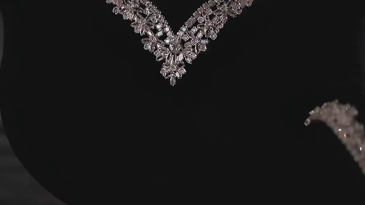 Close-up of the floral center of a V-shaped zircon necklace on black velvet, with part of the matching bracelet visible.