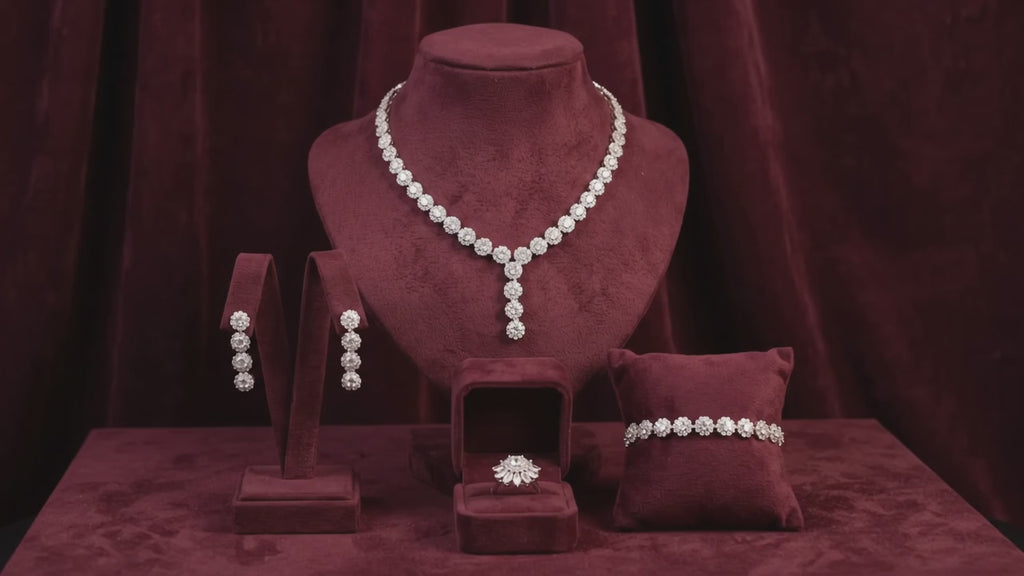 Mini flower bridal jewelry set with a Y-shaped necklace, matching drop earrings, bracelet and ring displayed on burgundy velvet.