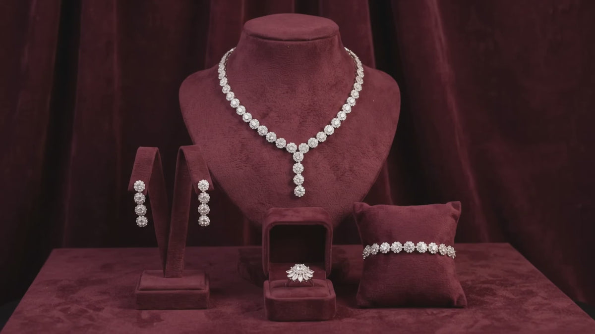Mini flower bridal jewelry set with a Y-shaped necklace, matching drop earrings, bracelet and ring displayed on burgundy velvet.