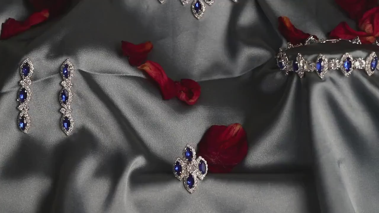 Blue zircon jewelry arranged on gray satin with red rose petals, showing the necklace and coordinating accessories.