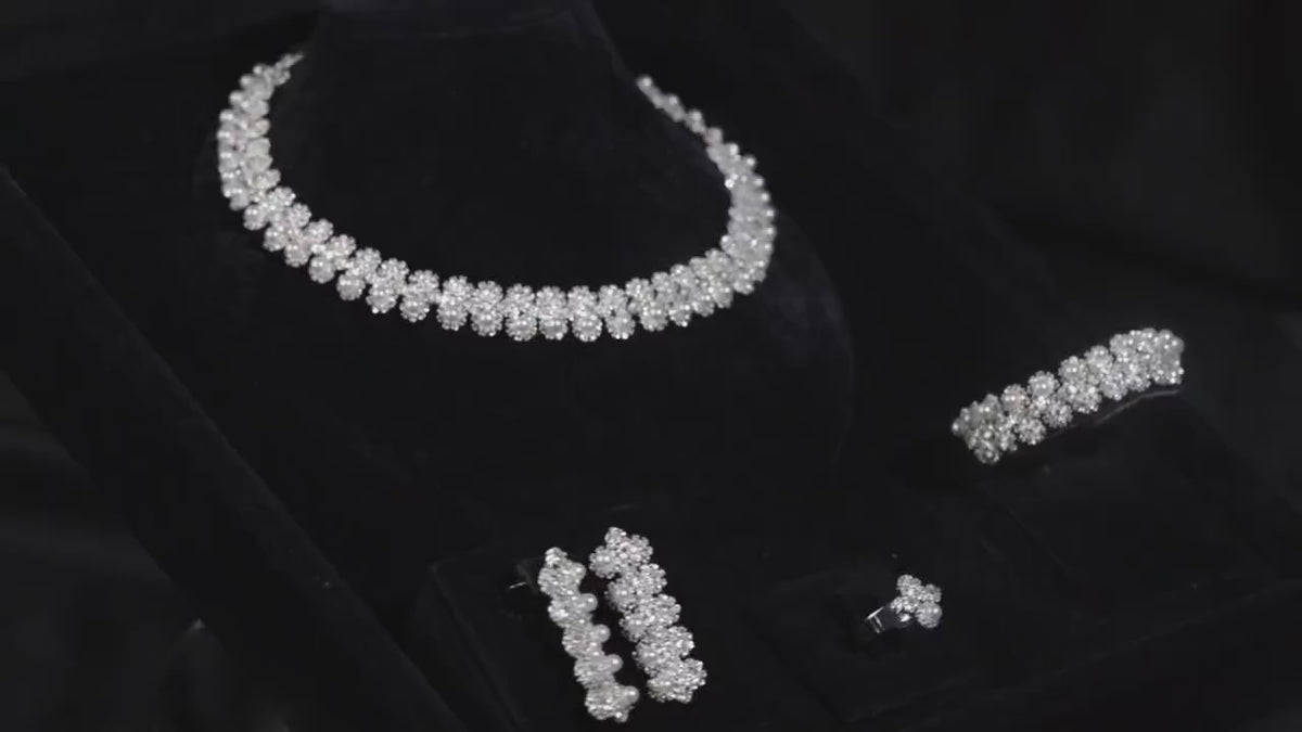 Silver-tone floral and faux pearl bridal jewelry set displayed on black velvet, with matching necklace, earrings, bracelet and ring.