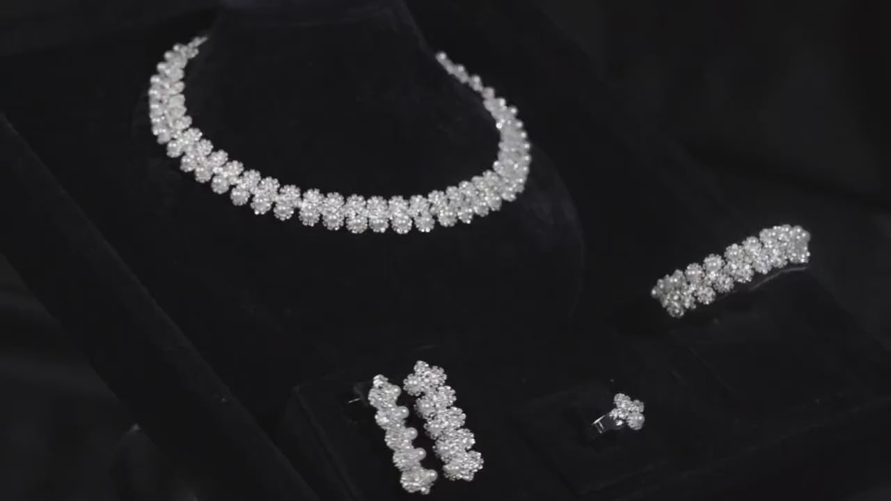 Silver-tone floral and faux pearl bridal jewelry set displayed on black velvet, with matching necklace, earrings, bracelet and ring.