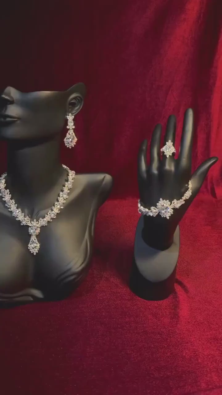 Silver-tone statement jewelry displayed on black necklace and hand stands against a red backdrop